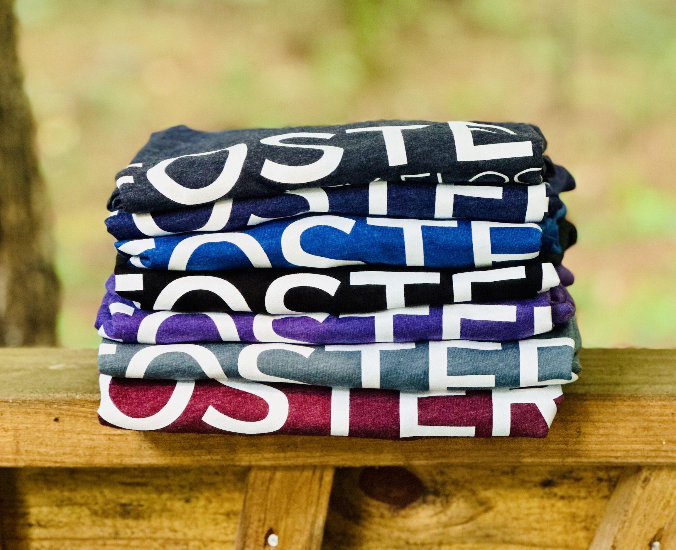 Folded tees printed at the shop, stacked in seven colours on a wooden rail